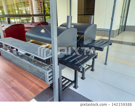 Outdoor grills set up near a building with seating area visible in a daytime setting Outdoor grills set up near a building with seating area visible in a daytime setting 142159388