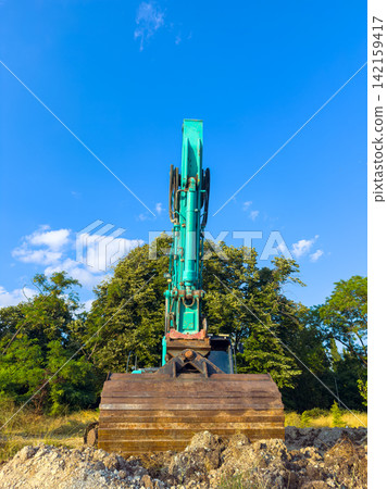 Heavy machinery digs up earth at a construction site under a clear blue sky in the late afternoon sunlight Heavy machinery digs up earth at a construction site under a clear blue sky in the late afternoon sunlight 142159417