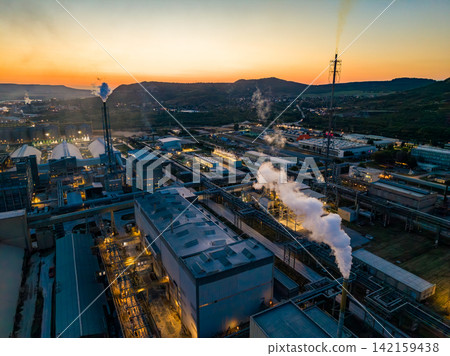 Industry facility with smoke stacks at sunset near hills and water Industry facility with smoke stacks at sunset near hills and water 142159438