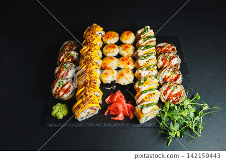 Sushi rolls and side dishes arranged on a black platter with wasabi and pickled ginger Sushi rolls and side dishes arranged on a black platter with wasabi and pickled ginger 142159443