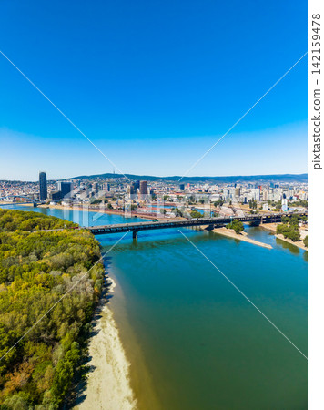 View of a city across a river with bridges and greenery under a clear sky View of a city across a river with bridges and greenery under a clear sky 142159478