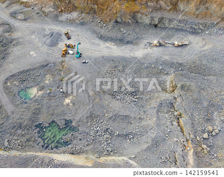 Workers operate machinery at a granite quarry in a remote area with large rocks and equipment visible on the ground 142159541