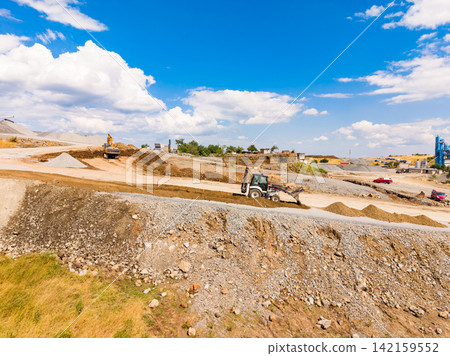 Granite quarry site with machinery working during the day under a blue sky with clouds Granite quarry site with machinery working during the day under a blue sky with clouds 142159552