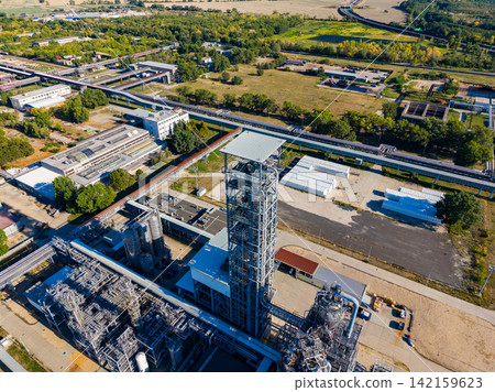 View of an industrial facility with large structures and surrounding green fields in a clear setting View of an industrial facility with large structures and surrounding green fields in a clear setting 142159623