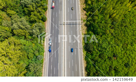 Traffic moves along a wide highway surrounded by trees in a rural area during bright daylight hours Traffic moves along a wide highway surrounded by trees in a rural area during bright daylight hours 142159649
