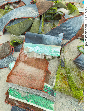 Old carpet pieces are stacked on a surface covered in sand at a construction site by the shore during a cloudy day Old carpet pieces are stacked on a surface covered in sand at a construction site by the shore during a cloudy day 142159659