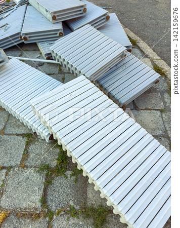 Wooden planks stacked in an outdoor area near a stone path in a sunny environment during daytime 142159676