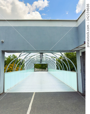Walkway connects two sides of a road under a blue sky with some clouds and green trees visible in the background Walkway connects two sides of a road under a blue sky with some clouds and green trees visible in the background 142159686