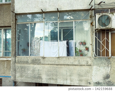 Curtains and clothes hang on a balcony of a residential building on a warm afternoon Curtains and clothes hang on a balcony of a residential building on a warm afternoon 142159688