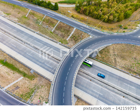 Traffic flows smoothly on a highway roundabout with a bus and a car navigating the road during daylight hours Traffic flows smoothly on a highway roundabout with a bus and a car navigating the road during daylight hours 142159735