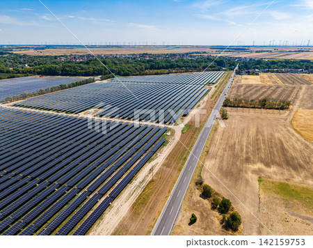 Large solar farm located near a rural area with a road and farmland in the background on a sunny day Large solar farm located near a rural area with a road and farmland in the background on a sunny day 142159753
