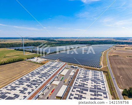Solar panels and wind turbines in a renewable energy area with fields and water in the background Solar panels and wind turbines in a renewable energy area with fields and water in the background 142159756
