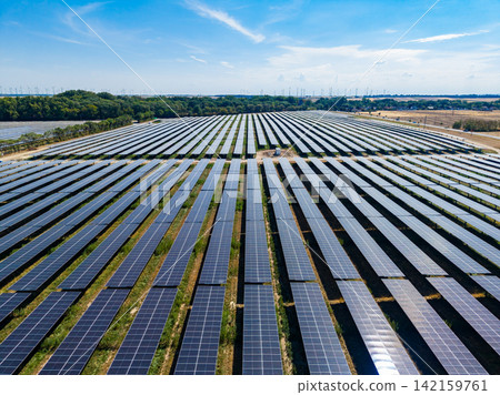 Solar panels cover a large area in an open field during the day with a clear sky and some clouds in the background Solar panels cover a large area in an open field during the day with a clear sky and some clouds in the background 142159761