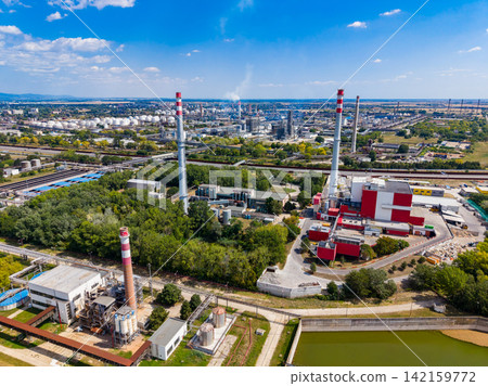 Factory site with large chimneys and green areas located near a city during daytime Factory site with large chimneys and green areas located near a city during daytime 142159772