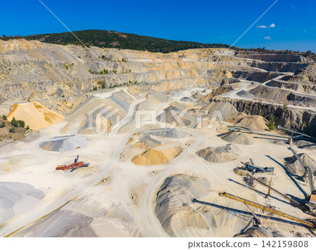 Large quarry site showing piles of different materials during daylight hours with clear blue sky and surrounding green hills Large quarry site showing piles of different materials during daylight hours with clear blue sky and surrounding green hills 142159808