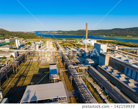 Factory area near water with clear sky and hills in the background during daytime Factory area near water with clear sky and hills in the background during daytime 142159939