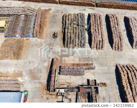Wood storage area contains many stacks of wood and machinery in a large open space during daylight hours 142159962