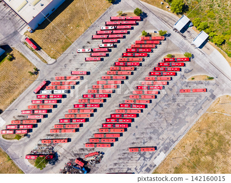 Large parking lot with numerous red buses arranged in rows during daylight hours at a transportation depot Large parking lot with numerous red buses arranged in rows during daylight hours at a transportation depot 142160015