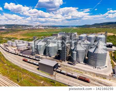 Grain storage facility with many silos located by train tracks in a rural area under a bright sky Grain storage facility with many silos located by train tracks in a rural area under a bright sky 142160250