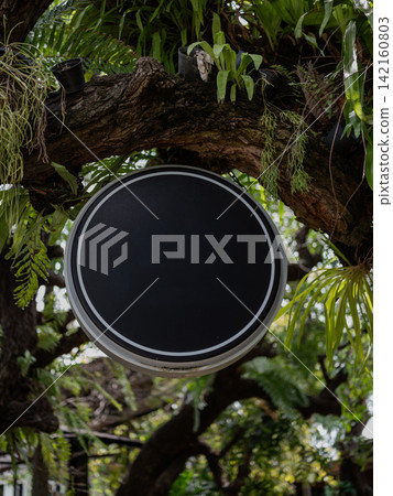 Blank round black hanging sign mockup under a large tree branch in a garden cafe. Blank round black hanging sign mockup under a large tree branch in a garden cafe. 142160803