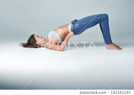Studio, fashion and woman with jeans for getting ready, dressing and challenge on grey background. Female person, denim and tight pants with struggle for weight gain, diet and stretching on floor Studio, fashion and woman with jeans for getting ready, dressing and challenge on grey background. Female person, denim and tight pants with struggle for weight gain, diet and stretching on floor 142161281