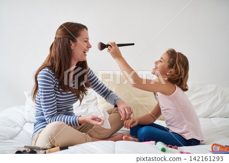 Mother, daughter and makeup in bedroom of home with cosmetic brush, playing and laughing with bonding. Family, woman and girl child with funny makeover for game, parenting and fun on bed of house Mother, daughter and makeup in bedroom of home with cosmetic brush, playing and laughing with bonding. Family, woman and girl child with funny makeover for game, parenting and fun on bed of house 142161293