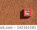 Red fire alarm manual call point on a textured orange wall 142161581