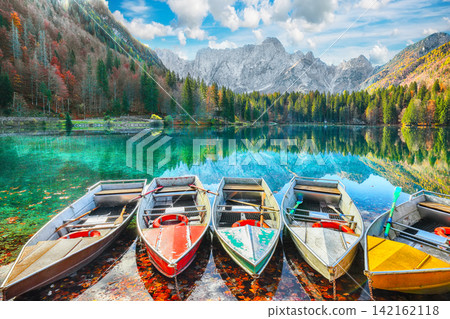 Remarkable view of Fusine lake with boats and Mangart peak on background. Remarkable view of Fusine lake with boats and Mangart peak on background. 142162118