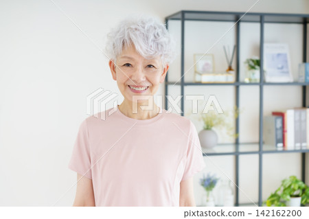 A portrait of a senior Japanese woman standing in her living room, smiling. A portrait of a senior Japanese woman standing in her living room, smiling. 142162200