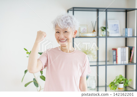 A portrait of a senior Japanese woman making a victory pose in her living room. A portrait of a senior Japanese woman making a victory pose in her living room. 142162201