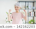 A portrait of a senior Japanese woman making a victory pose in her living room. A portrait of a senior Japanese woman making a victory pose in her living room. 142162203