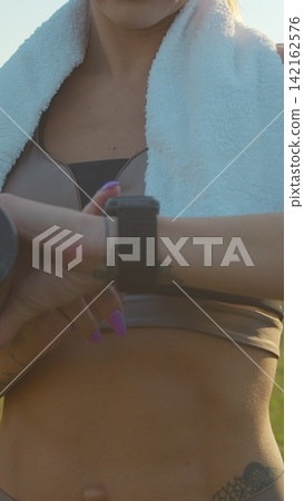 Vertical video. Woman tracking her running progress with a smartwatch in the city stadium. Vertical video. Woman tracking her running progress with a smartwatch in the city stadium. 142162576