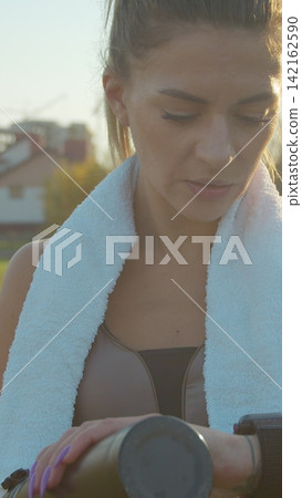 Vertical video. Woman tracking her running progress with a smartwatch in the city stadium. Vertical video. Woman tracking her running progress with a smartwatch in the city stadium. 142162590