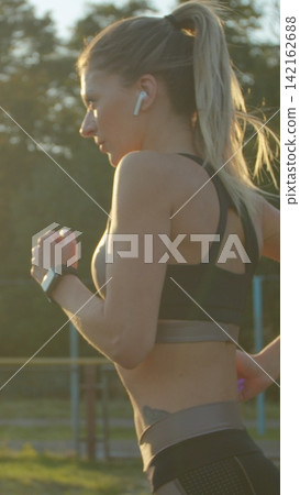 Vertical video. Pretty sporty woman running in the sports stadium with earphones listening to music. Vertical video. Pretty sporty woman running in the sports stadium with earphones listening to music. 142162688