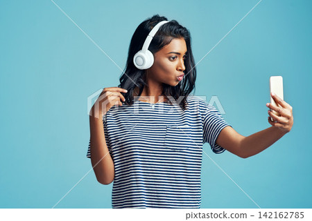 Fashion, music and selfie of woman in studio for social media isolated on blue background. Photography, headphones and Indian girl in casual clothes or influencer listening to kpop on mockup space Fashion, music and selfie of woman in studio for social media isolated on blue background. Photography, headphones and Indian girl in casual clothes or influencer listening to kpop on mockup space 142162785
