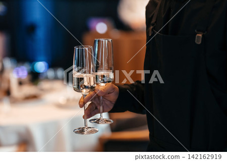 Professional waiter serving champagne glasses in luxury restaurant or event venue Professional waiter serving champagne glasses in luxury restaurant or event venue 142162919