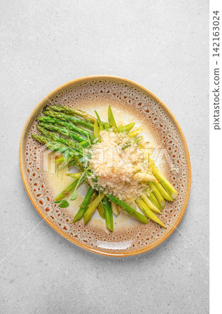 Fresh green asparagus spears arranged on a decorative plate with breadcrumbs and herbs, served on a light gray surface for a culinary presentation Fresh green asparagus spears arranged on a decorative plate with breadcrumbs and herbs, served on a light gray surface for a culinary presentation 142163024