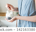 Woman stirs yogurt and berries in a glass 142163380