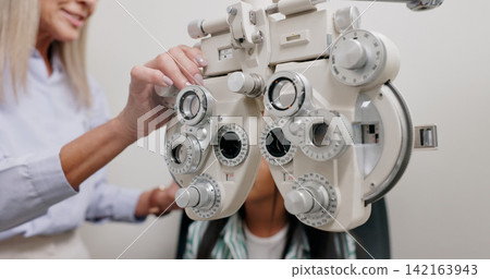Eye care, medical and child in clinic, hand and test of specialist, phoropter or refractor for girl. Healthcare, technology and machine for help for kid, exam and vision for check up in hospital 142163943