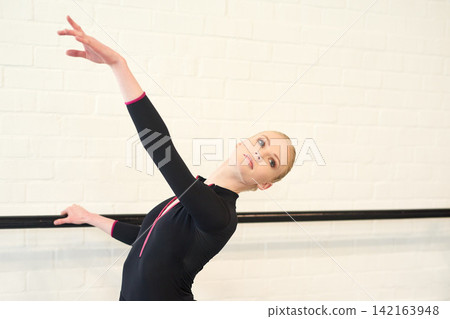 Woman, ballet and dancer in studio for fitness, exercise and training for performance or show. Young female ballerina, rehearsal and elegant indoor at school of art for creative, artist and barre Woman, ballet and dancer in studio for fitness, exercise and training for performance or show. Young female ballerina, rehearsal and elegant indoor at school of art for creative, artist and barre 142163948