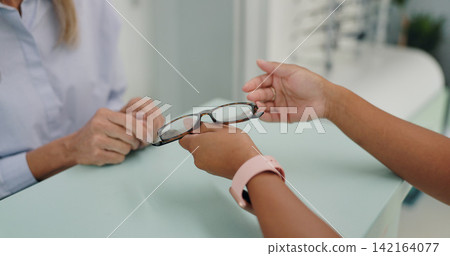Glasses, frame and hands of patient at counter by employee in clinic for vision, prescription or eye care. Optometrist, healthcare or lens or health for eyes, glaucoma and ocular diseases or eyesight Glasses, frame and hands of patient at counter by employee in clinic for vision, prescription or eye care. Optometrist, healthcare or lens or health for eyes, glaucoma and ocular diseases or eyesight 142164077