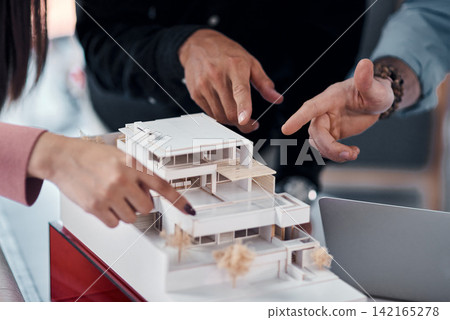 Hands, architect group and model of building with pointing for ideas, advice or planning for construction. People, engineering and property developer team in office with vision, design or creativity 142165278