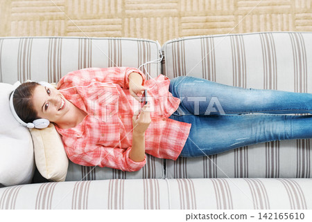 Happy woman, portrait and headphones with phone above in relax on sofa for music, podcast or audio streaming at home. Top view of young female person with smile on mobile smartphone for entertainment 142165610