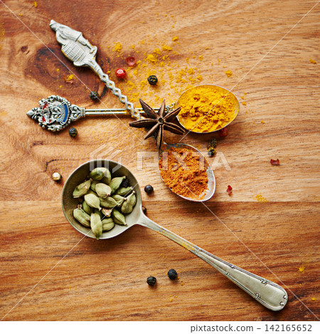 Spoons, spice and selection of color for seasoning on kitchen table, turmeric and cardamom for meal. Top view, condiments and options for spicy cooking in Indian culture, nutmeg and food preparation Spoons, spice and selection of color for seasoning on kitchen table, turmeric and cardamom for meal. Top view, condiments and options for spicy cooking in Indian culture, nutmeg and food preparation 142165652