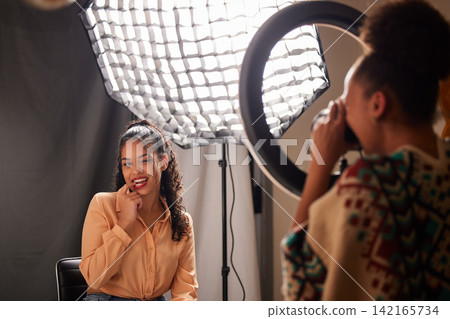 Model, photographer and ring light for fashion influencer and photography in creative studio and agency. Woman, camera and lighting gear with professional shooting session for magazine photoshoot Model, photographer and ring light for fashion influencer and photography in creative studio and agency. Woman, camera and lighting gear with professional shooting session for magazine photoshoot 142165734