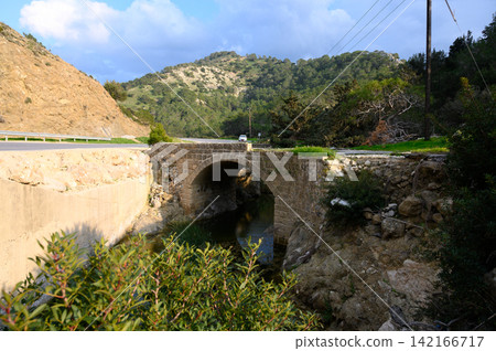 Exploring the historic stone bridge over the tranquil stream in the mountain landscape during a sunny afternoon Exploring the historic stone bridge over the tranquil stream in the mountain landscape during a sunny afternoon 142166717