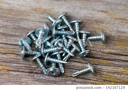 Array of shiny metal screws scattered across a rustic wooden surface highlighting craftsmanship and tools in construction projects Array of shiny metal screws scattered across a rustic wooden surface highlighting craftsmanship and tools in construction projects 142167129