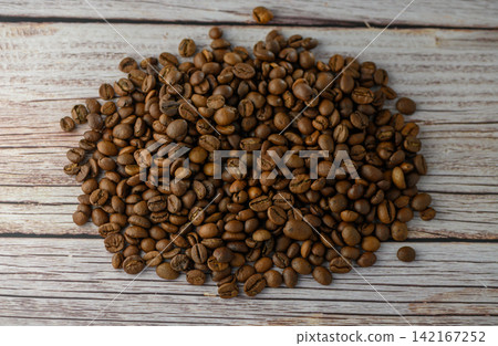 Scattered heap of roasted coffee beans on light wooden surface top view Scattered heap of roasted coffee beans on light wooden surface top view 142167252
