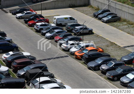 Busy parking lot filled with a variety of cars showcasing vibrant colors and sleek designs under a clear blue sky Busy parking lot filled with a variety of cars showcasing vibrant colors and sleek designs under a clear blue sky 142167280