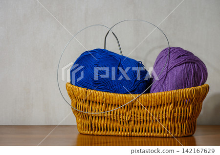Wicker basket with blue and violet yarn skeins and circular knitting pins Wicker basket with blue and violet yarn skeins and circular knitting pins 142167629